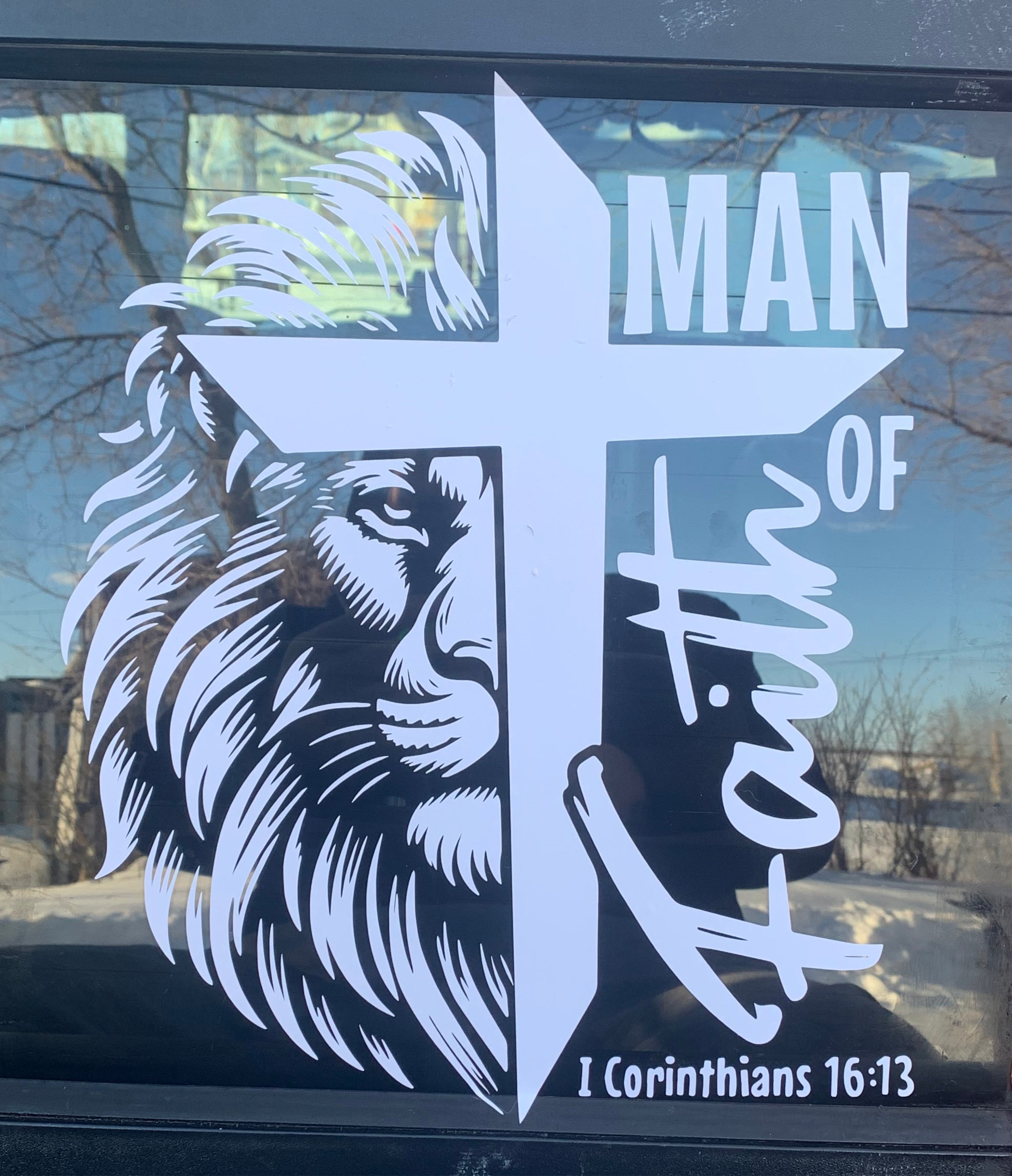 Decal with lion head, cross, and 'Man of Faith' text on a car window.