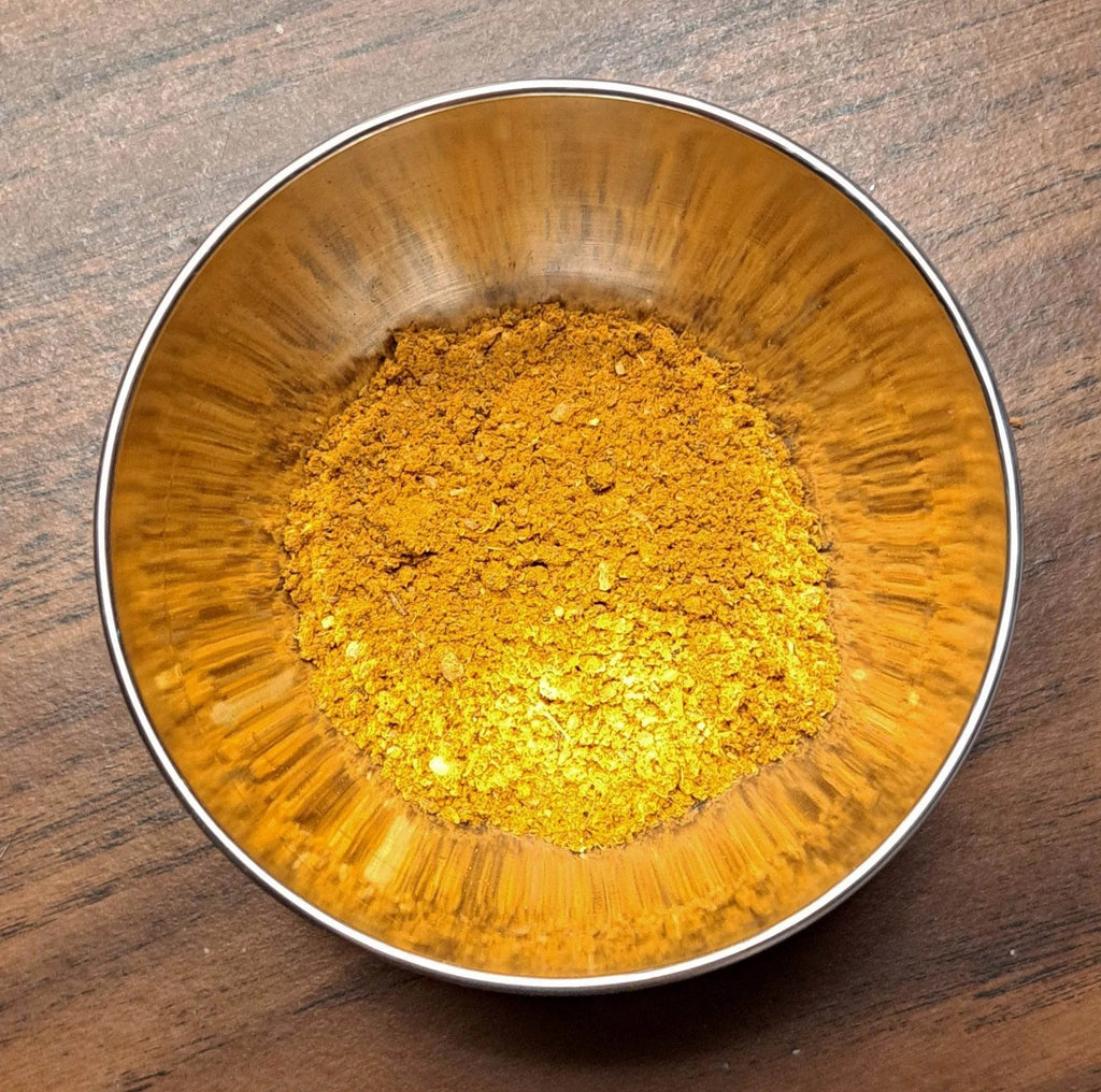 Metallic bowl filled with Curry powder on a wooden surface