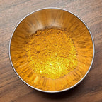 Metallic bowl filled with Curry powder on a wooden surface