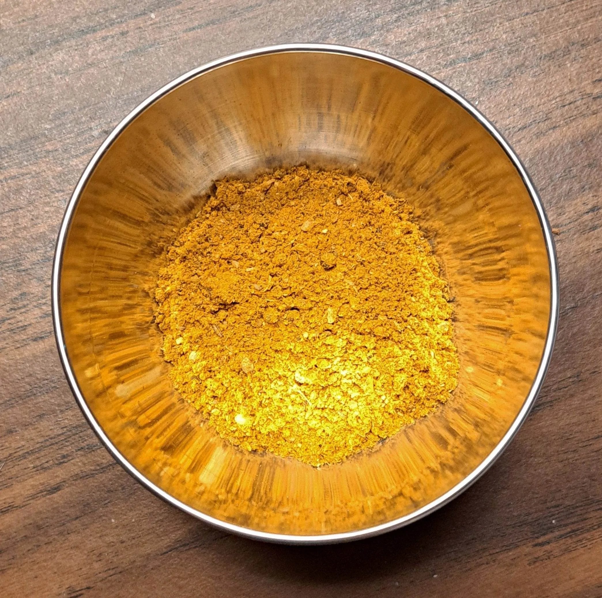 Metallic bowl filled with Curry powder on a wooden surface