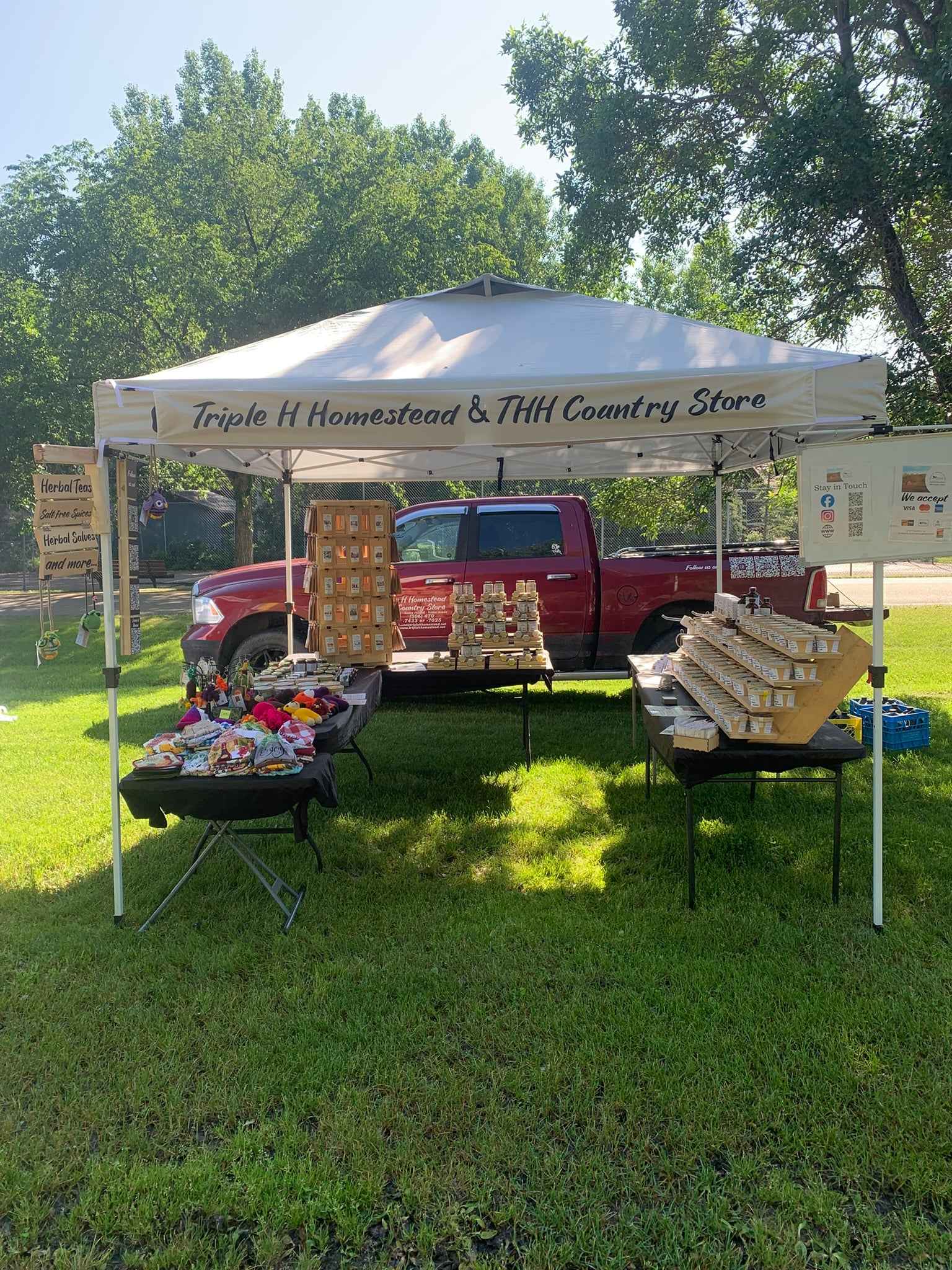 Red truck under a white tent with 'Triple H Homestead & THH Country Store' branding, set up outdoors on grass.