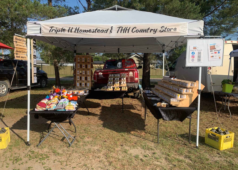Outdoor setup with a tent labeled 'Triple H Homestead & TTH Country Store' displaying various items.