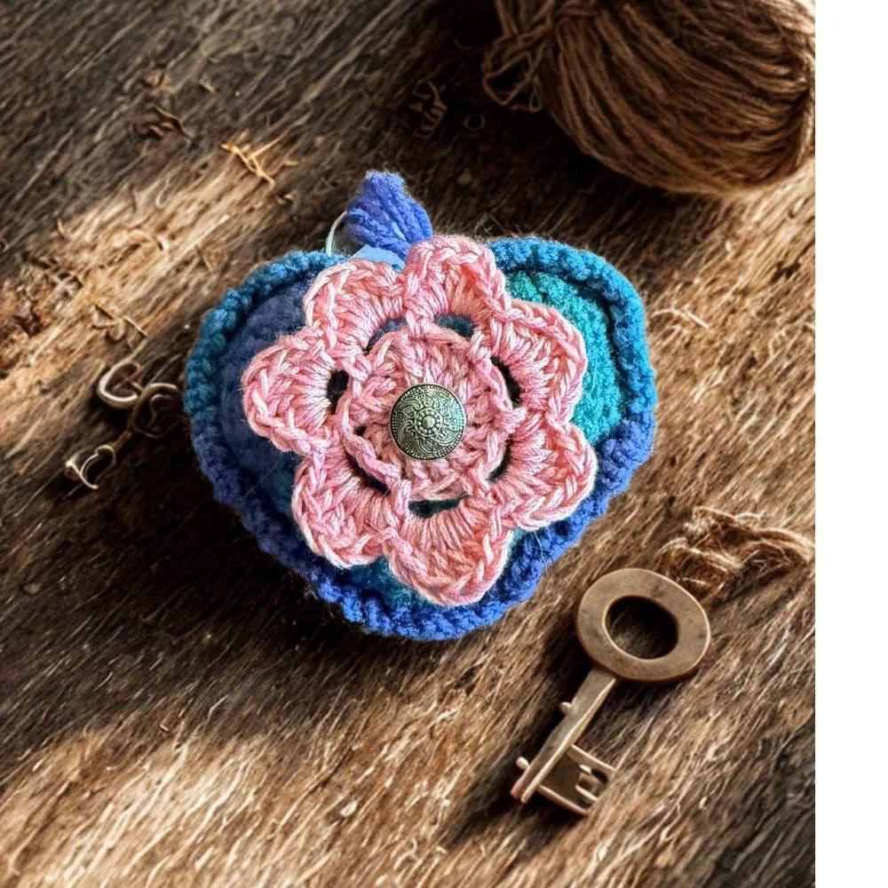 Crocheted flower keychain on a wooden surface with a key and yarn ball.