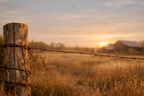 Barbed wire fence with sunset over a field and barn in the background