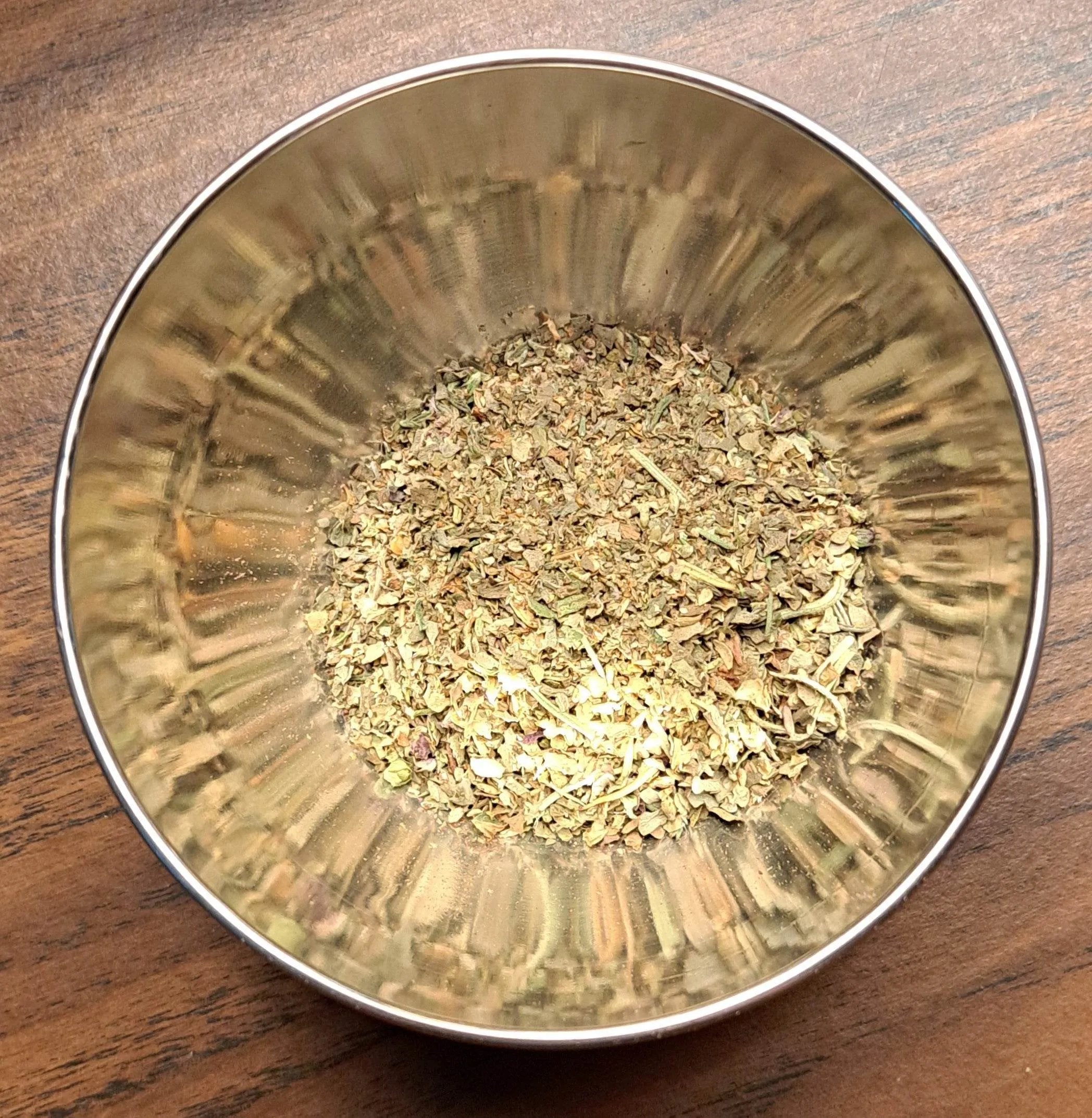 Metallic bowl with Italian Seasoning on a wooden surface