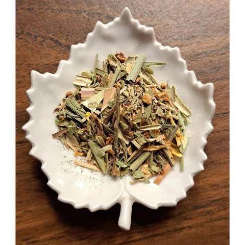 Lemony Kiss Herbal tea leaves in a white ceramic leaf-shaped bowl on a wooden surface