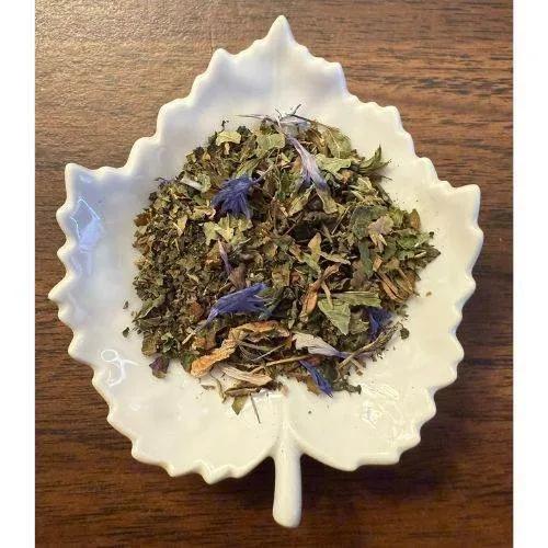 Living Sky Herbal tea leaves in a white ceramic leaf-shaped bowl on a wooden surface