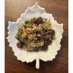 White leaf-shaped bowl filled with Lower the Pressure dried herbs on a wooden surface