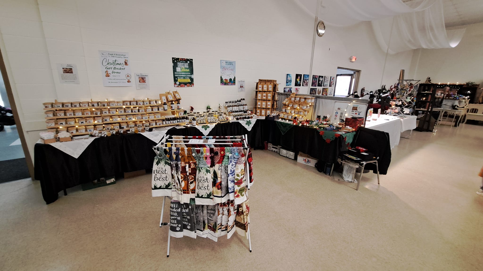 Display of products on tables and racks in a room with white walls and carpeted floor.