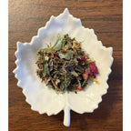 Nourishing Ice Tea Herbal mix in a white leaf-shaped bowl on a wooden surface