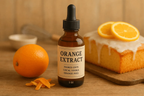 Bottle of orange extract with an orange, peel, and cake on a wooden surface