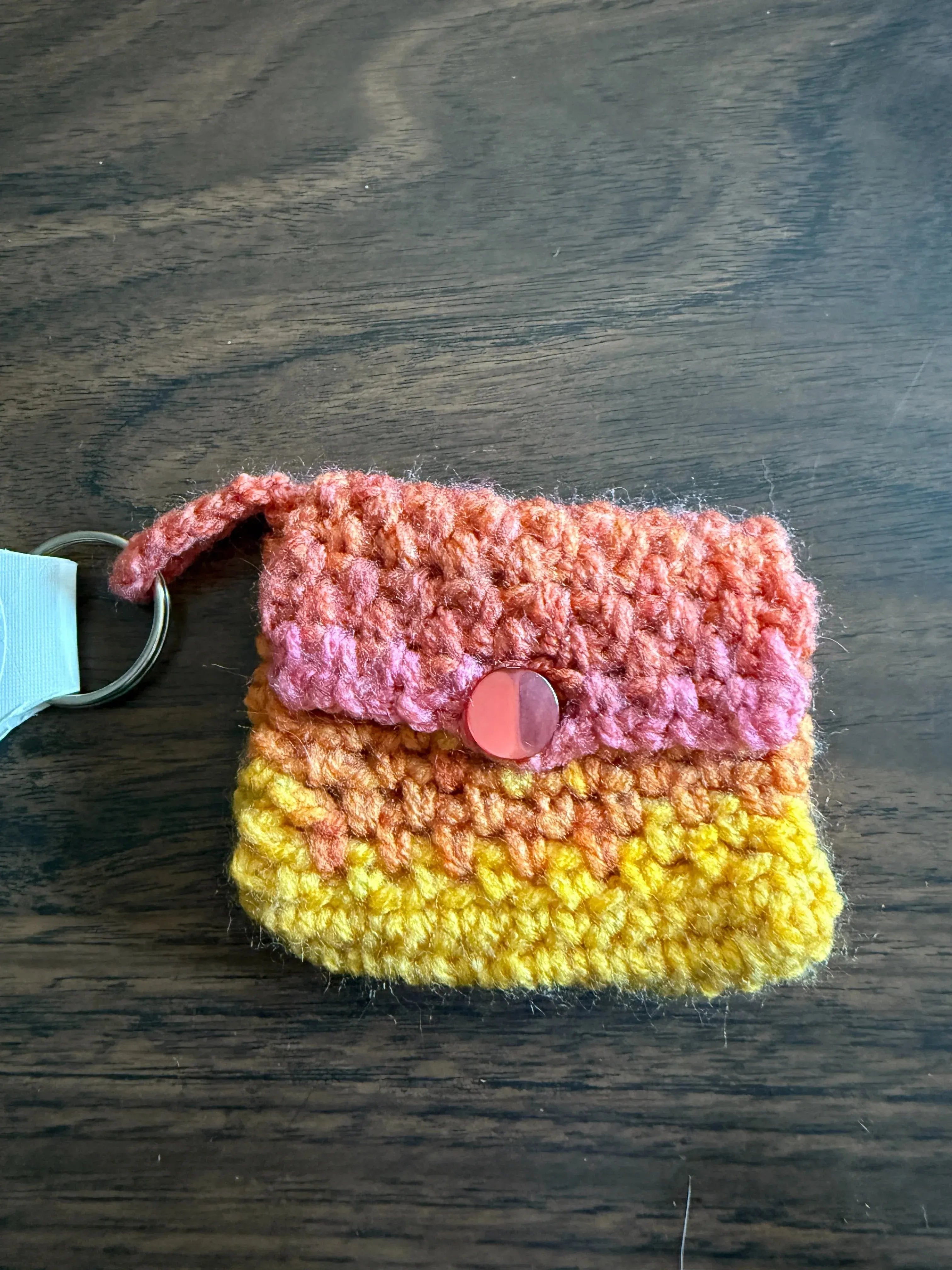 Crocheted keychain pouch with pink and yellow colors on a wooden surface