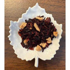 Red Fruit Happy Tea Tea leaves with apple pieces on a white leaf-shaped dish on a wooden surface