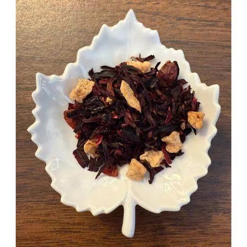 Red Fruit Happy Tea Tea leaves with apple pieces on a white leaf-shaped dish on a wooden surface