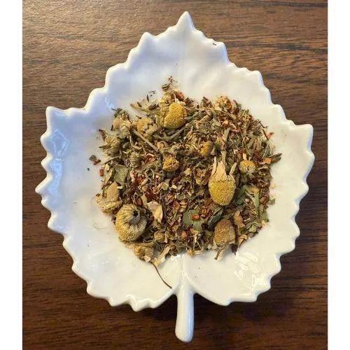 Sip & Soothe Herbal tea mix in a white leaf-shaped bowl on a wooden surface