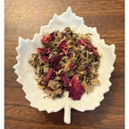 White leaf-shaped bowl filled with dried herbs and flowers on a wooden surface