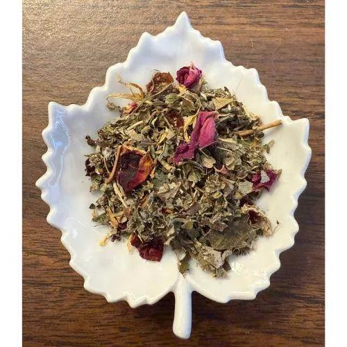 Snuggle Brew tea mix with dried leaves and flowers in a white leaf-shaped bowl on a wooden surface