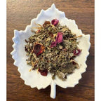 Snuggle Brew tea mix with dried leaves and flowers in a white leaf-shaped bowl on a wooden surface