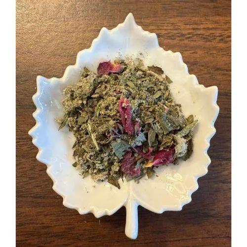 Splendid Women's Tea Herbal mix with pink flowers on a white leaf-shaped dish on a wooden surface