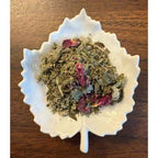 Splendid Women's Tea Herbal mix with pink flowers on a white leaf-shaped dish on a wooden surface