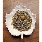 Stress Relief Herbal tea leaves in a white leaf-shaped bowl on a wooden surface