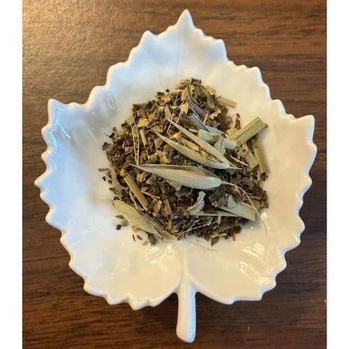White leaf-shaped bowl filled with Thirst Quencher herbs on a wooden surface