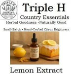 Triple H Country Essentials lemon extract bottle with lemons and a cake on a wooden surface.