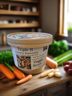Triple H Country Essentials Veggie Broth container on a wooden surface with vegetables in the background